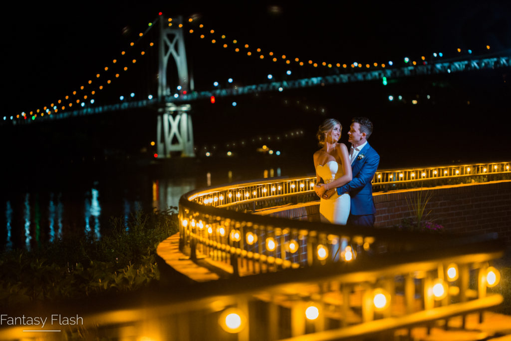 A well lit bridge in the background of a newly married couple posing for a wedding photo