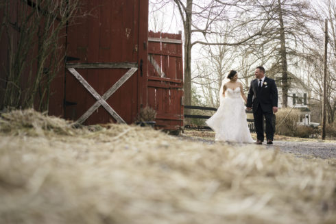 couple posing for wedding photos by a red barn