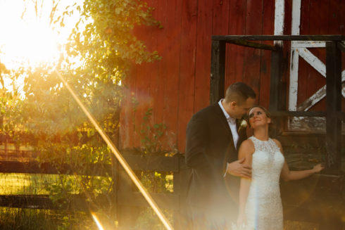bride and groom posing in front of red barn