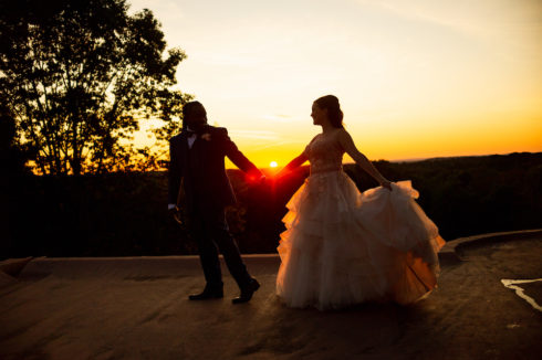 bride and groom holding hands with sun setting