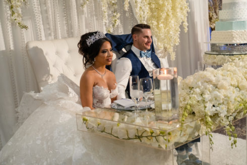 bride and groom sitting at flower covered dais