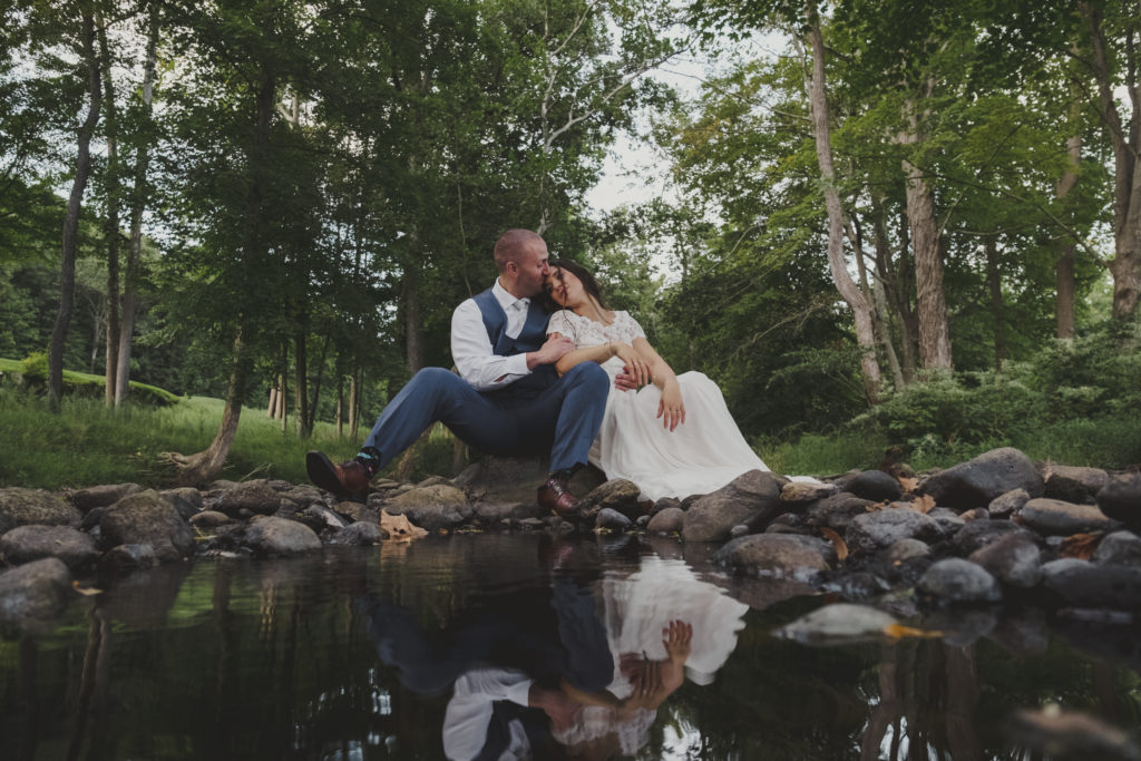 A bride and groom sitting by a small pond at Hollow Brook