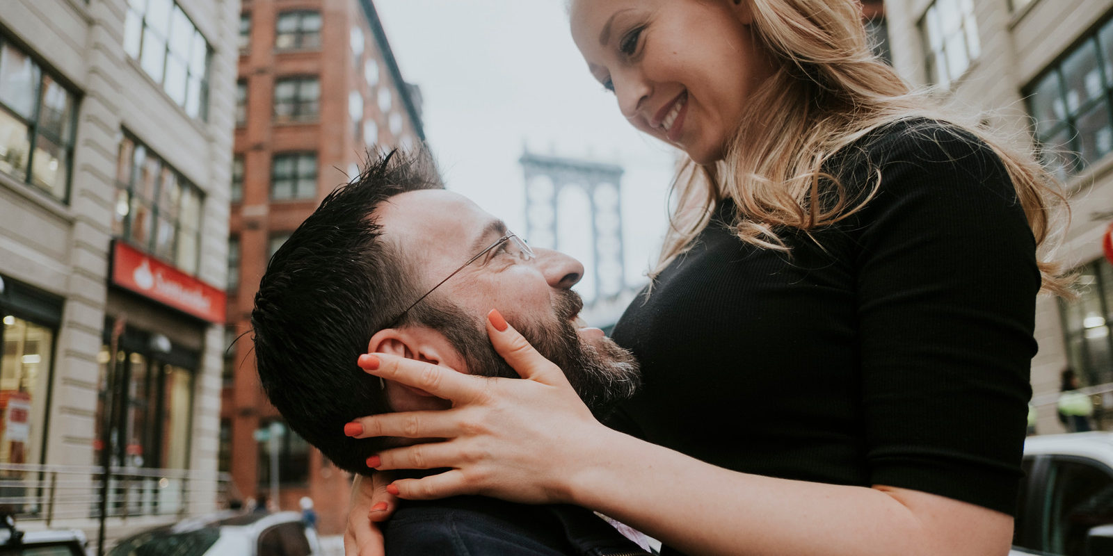 featured This is a couple embracing each other in the middle of the street in Brooklyn. The man is lifting his partner in the air and she smiles down on him.