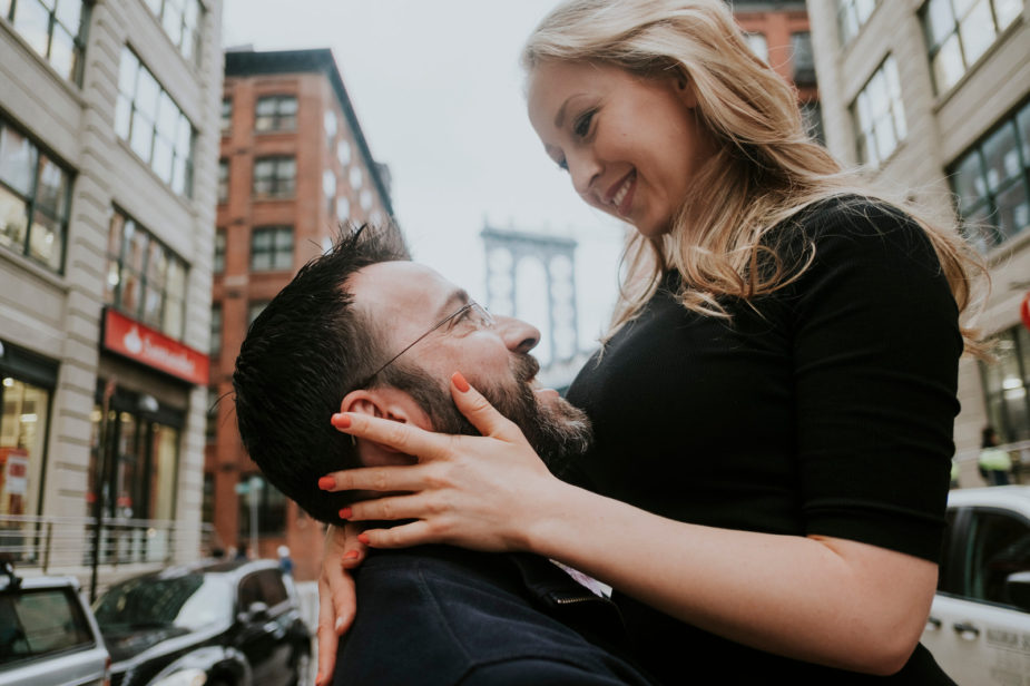 This is a couple embracing each other in the middle of the street in Brooklyn. The man is lifting his partner in the air and she smiles down on him.